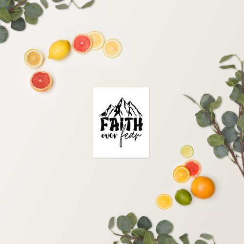 A "Faith Over Fear" poster, featuring a white background with a mountain graphic and the text "FAITH over fear" in black, is shown centered against a light backdrop. The display is surrounded by green eucalyptus leaves and an assortment of citrus fruits, including lemons, limes, oranges, and grapefruit. This poster makes for inspiring religious gifts that convey Jesus' message perfectly. christian gifts, religious gifts, gifts of faith, faith based gifts, faith inspired gifts