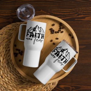 Overhead view of a round wooden tray holding two Faith Over Fear Travel Mugs on a woven placemat. The mugs display the text "Faith over fear" with an illustration of mountains. Coffee beans are scattered around the tray, and one mug has its lid off and placed beside it—ideal religious gifts for any occasion. christian gifts, religious gifts, gifts of faith, faith based gifts, faith inspired gifts