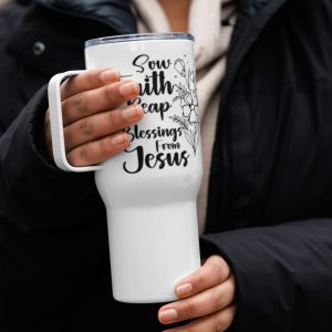 A person wearing a dark jacket holds a white Sow Faith Reap Blessing From Jesus Travel Mug with a handle. The mug features decorative text saying, "Sow with reap blessings from Jesus," alongside illustrations of flowers and leaves. christian gifts, religious gifts, gifts of faith, faith based gifts, faith inspired gifts