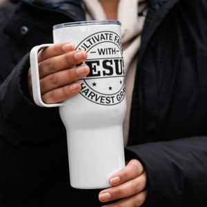 A person dressed in dark outerwear holds a white Cultivate Faith With Jesus Harvest Grace Travel Mug with a black printed design. The design includes circular text that says, "CULTIVATE FA..." at the top and "...HARVEST GRACE" at the bottom, with "JESU..." prominently displayed in the center. christian gifts, religious gifts, gifts of faith, faith based gifts, faith inspired gifts