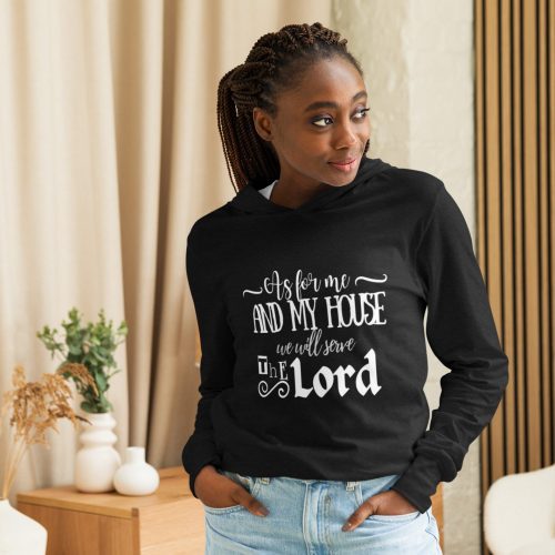 A woman wearing the "As For Me We Will Serve The Lord Hoodie" in black stands in a cozy room, where plants adorn white vases on a wooden table. She gazes thoughtfully to the side. christian gifts, religious gifts, gifts of faith, faith based gifts, faith inspired gifts