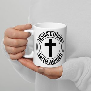 A person wearing a white long-sleeve shirt is holding the Jesus Guides Faith Abides Coffee Cup, which is white with black text and a cross symbol. The text reads "JESUS GUIDES FAITH ABIDES" encircling the cross. Only the person's hands and part of the torso are visible, showcasing one of many cherished Christian gifts celebrating faith. christian gifts, religious gifts, gifts of faith, faith based gifts, faith inspired gifts