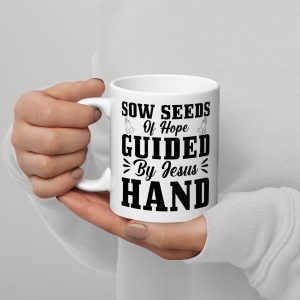 A person wearing a white long-sleeve shirt holds the "Sow Seeds Of Hope Guided By Jesus' Hand Coffee Cup," which features black text that reads, "Sow seeds of hope guided by Jesus' hand," adorned with small illustrated doves. Their nails are painted light beige—a perfect choice for religious gifts or meaningful Christian gifts. christian gifts, religious gifts, gifts of faith, faith based gifts, faith inspired gifts