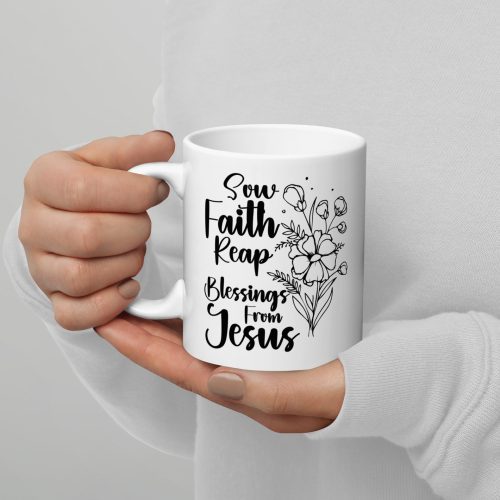 A person wearing a white sweater holds the "Sow Faith Reap Blessing From Jesus Coffee Cup," which features black text that reads, "Sow Faith Reap Blessings from Jesus," alongside an illustrated bouquet of flowers on the right side—making it a perfect addition to any collection of religious gifts. christian gifts, religious gifts, gifts of faith, faith based gifts, faith inspired gifts