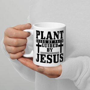 A person wearing a white long-sleeve shirt holds the "Plant Seeds Of Faith Guided By Jesus Coffee Cup," adorned with black text reading, "Plant seeds of faith guided by Jesus" surrounded by four crosses, making it one of the perfect gifts of faith. christian gifts, religious gifts, gifts of faith, faith based gifts, faith inspired gifts