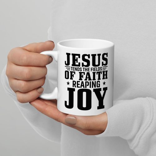 A person holding a Jesus Tends The Fields Of Faith Reaping Joy Coffee Cup, featuring black text with the message, "Jesus tends the fields of faith reaping joy," showcasing one of the thoughtful Judeo Gifts. The person is wearing a white long-sleeved shirt, and only their hands are visible in the image. christian gifts, religious gifts, gifts of faith, faith based gifts, faith inspired gifts