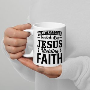 A person wearing a white long-sleeve shirt holds the "Heart's Garden Tended By Jesus Yielding Faith Coffee Cup" from the collection of Christian gifts. The mug features a black text design that reads, "Heart's Garden Tended By Jesus Yielding Faith. christian gifts, religious gifts, gifts of faith, faith based gifts, faith inspired gifts