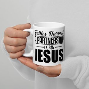 A person holding the "Faiths Harvest A Partnership With Jesus Coffee Cup" with both hands. The white ceramic mug features bold black text that reads "Faith's Harvest A Partnership With Jesus." The person, wearing a light-colored long-sleeve shirt, showcases one of the cherished Christian gifts perfect for any faithful occasion. christian gifts, religious gifts, gifts of faith, faith based gifts, faith inspired gifts