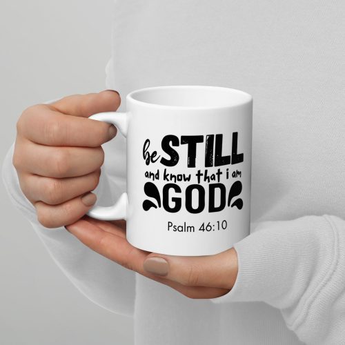 A person wearing a white sweater and a Christian T-Shirt holds a Be Still and Say that I Am God "Psalm 46:10" Coffee Cup with both hands. This makes for one of the perfect Christian gifts or gifts of faith. christian gifts, religious gifts, gifts of faith, faith based gifts, faith inspired gifts