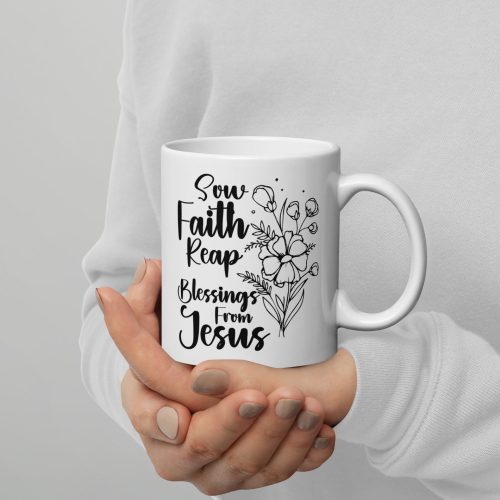 A person in a white sweater holds the "Sow Faith Reap Blessing From Jesus Coffee Cup," a white ceramic mug adorned with a floral design and the inspiring text written in black script. This beautiful piece from Judeo Gifts is perfect for those who cherish gifts of faith. The background is plain and grey. christian gifts, religious gifts, gifts of faith, faith based gifts, faith inspired gifts