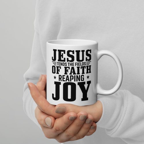 A person in a light-colored sweater holds the "Jesus Tends The Fields Of Faith Reaping Joy Coffee Cup," a white mug adorned with black text that reads, "Jesus tends the fields of faith reaping joy," accented with decorative stars. Perfect for those seeking meaningful Christian gifts, their nails are painted in a neutral shade. christian gifts, religious gifts, gifts of faith, faith based gifts, faith inspired gifts