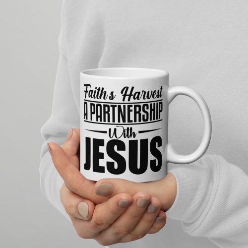 A person in a white sweater is holding the Faiths Harvest A Partnership With Jesus Coffee Cup, which features black text that reads "Faith’s Harvest A Partnership With Jesus." The plain, light-colored background highlights this perfect Christian gift and its heartfelt message. christian gifts, religious gifts, gifts of faith, faith based gifts, faith inspired gifts