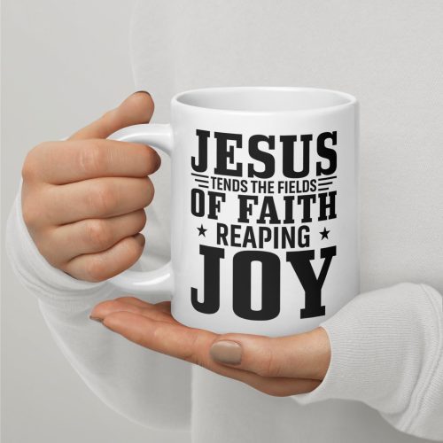 A person holds the "Jesus Tends The Fields Of Faith Reaping Joy Coffee Cup," a white mug adorned with bold black text that beautifully states, "JESUS TENDS THE FIELDS OF FAITH REAPING JOY." Dressed in a long-sleeved white shirt, they exhibit one of the perfect Christian gifts for spreading faith. christian gifts, religious gifts, gifts of faith, faith based gifts, faith inspired gifts