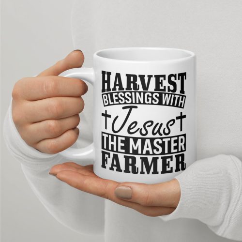 A person in a white, long-sleeve shirt holds a "Harvest Blessing With Jesus The Master Farmer Coffee Cup," which features black text reading "Harvest Blessings with Jesus, the Master Farmer." Crosses accompany the word "Jesus," making it one of those perfect gifts of faith. christian gifts, religious gifts, gifts of faith, faith based gifts, faith inspired gifts