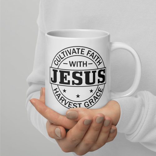 A person wearing a white long-sleeve shirt holds the "Cultivate Faith With Jesus Harvest Grace Coffee Cup," one of many thoughtful Judeo Gifts. The mug features black text that reads "Cultivate Faith with Jesus" and "Harvest Grace" within a circular design adorned with stars. The person's fingernails are painted beige. christian gifts, religious gifts, gifts of faith, faith based gifts, faith inspired gifts