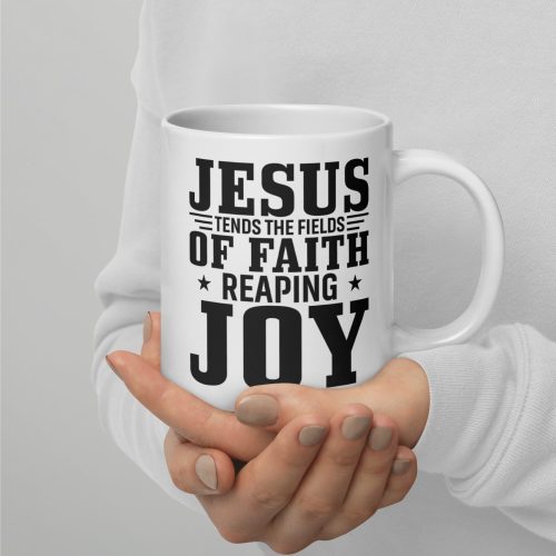 A person in a white long-sleeve shirt holds the "Jesus Tends The Fields Of Faith Reaping Joy Coffee Cup," featuring bold black text that reads, "JESUS TENDS THE FIELDS OF FAITH REAPING JOY." Their nails are painted a light gray color, accentuating the spiritual warmth of Judeo Gifts. christian gifts, religious gifts, gifts of faith, faith based gifts, faith inspired gifts